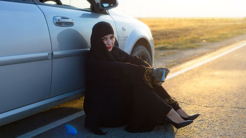Full length of woman in burka sitting by car on road