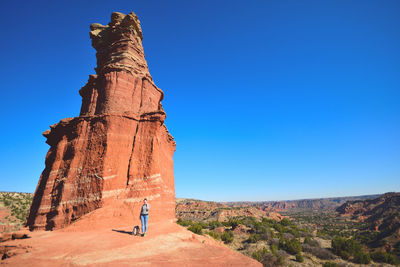 Young woman standing by rock formation against clear blue sky