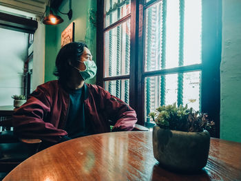 Young man looking through window at home