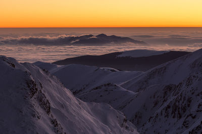 Scenic view of snow covered mountains against sky at sunset