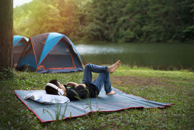 Holiday camping - young boy resting on pallet near a tent in the forest