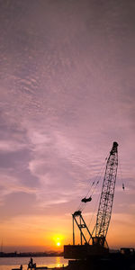 Silhouette cranes at construction site against sky during sunset