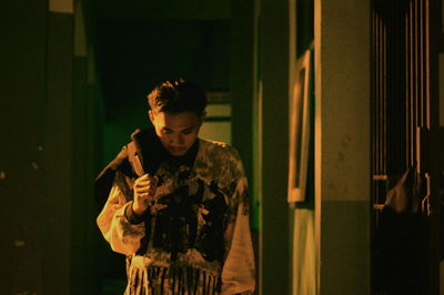 Man holding camera while standing against wall at night