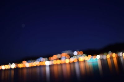 Defocused image of illuminated lights against sky at night