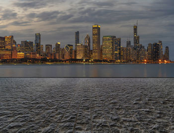 Illuminated buildings in city against cloudy sky