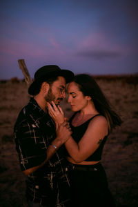 Young couple standing on land against sky during sunset