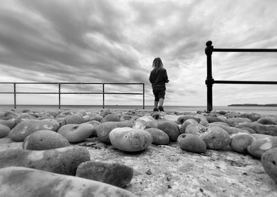 Rear view of child standing on rocks by sea against sky