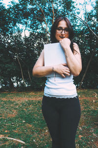 Portrait of young woman holding book while standing at park