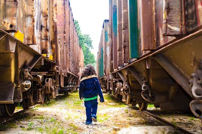 Rear view of girl walking amidst rusty freight trains
