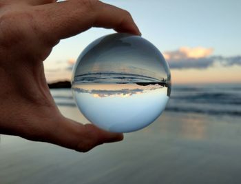 Cropped image of hand holding crystal ball against sky