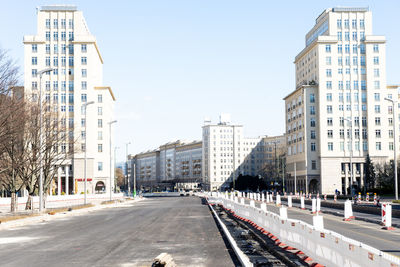 Road by buildings in city against clear sky