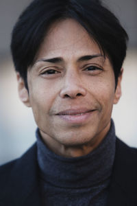 Positive ethnic male with short black hair in jacket and turtleneck sweater looking at camera