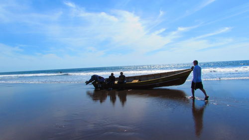 People by boat on beach against sky