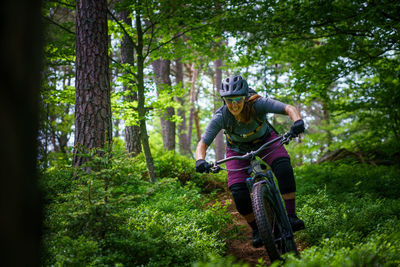 Woman riding mountain bike on footpath amidst trees in forest, austria
