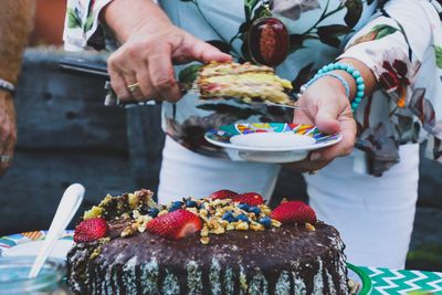 Midsection of woman serving cake in plate