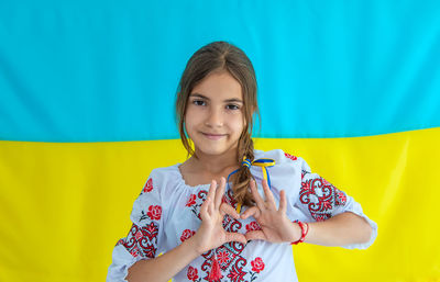 Smiling girl gesturing heart shape against ukrainian flag
