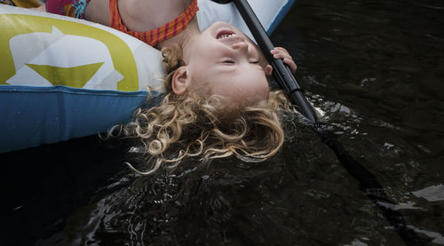 High angle view of happy cute girl lying in inflatable raft on lake