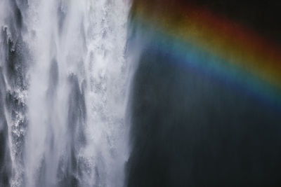 Breathtaking scenery of rainbow shining over rapid powerful skogafoss waterfall flowing through rocky cliff in iceland