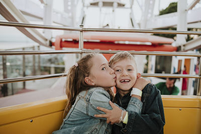 Girl kissing brother sitting in ferris wheel at amusement park