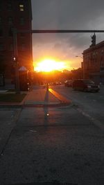 City street by buildings against sky during sunset