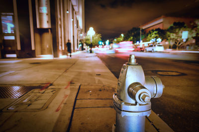 Fire hydrant on city street at night, buildings and light trails in distance