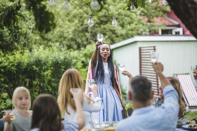 Smiling woman toasting drink with friends and family in backyard during weekend party