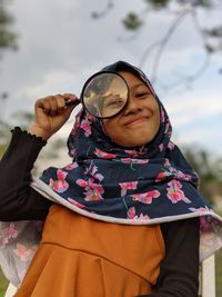 Portrait of young woman holding magnifying glass standing outdoors