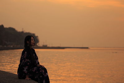 Woman sitting at beach against sky during sunset