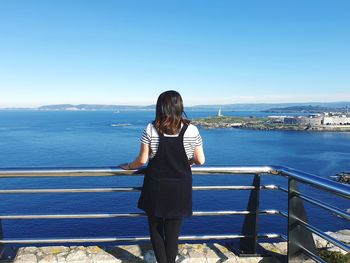 Rear view of woman standing on railing against sea