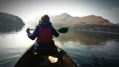 Rear view of woman boating in lake against mountains