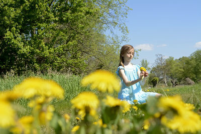 Girl holding flower on field during sunny day