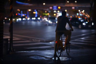 Rear view of man riding bicycle on city street at night