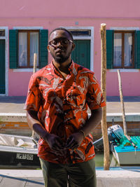 Portrait of man standing against canal and house in city