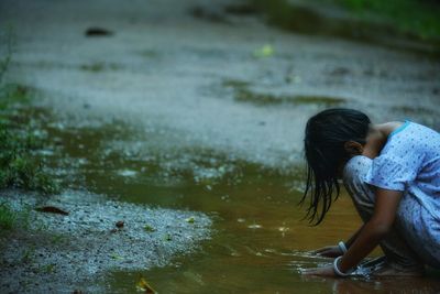 Full length of girl playing in puddle while couching on road