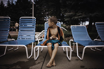 Boy sitting on lounge chair at poolside