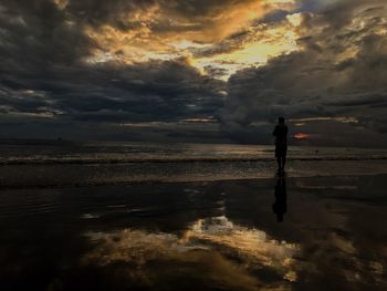 Silhouette of man on lake against dramatic sky