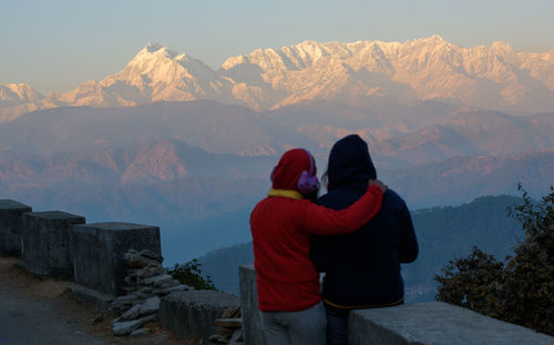 Rear view of couple standing against snowcapped mountain during sunset