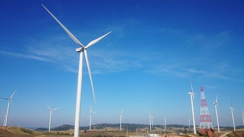 Low angle view of wind turbines on field against blue sky