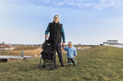 Grandfather holding hands of granddaughter while walking on grassy field