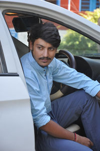 Closeup of a young indian guy looking sideways while sitting in the car with open door 