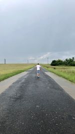 Full length rear view of man walking on road against sky