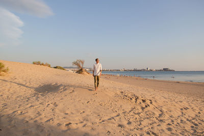 Rear view of woman walking at beach against clear sky