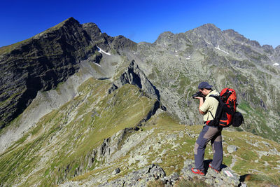 Side view of backpack man photographing through camera on top of mountain