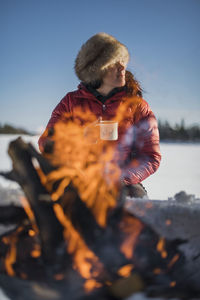 Woman holding mug near campfire