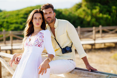 Portrait of man sitting on railing with woman outdoors