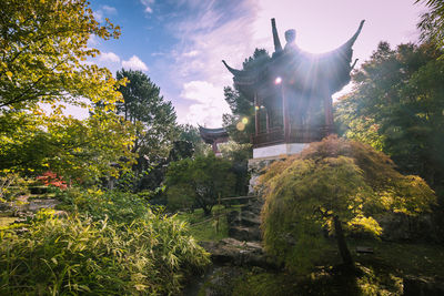 Low angle view of statue amidst plants against sky