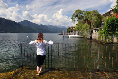 Rear view of woman standing by sea against sky