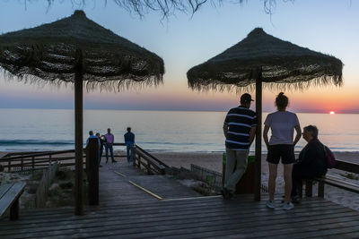 People at beach against sky during sunset