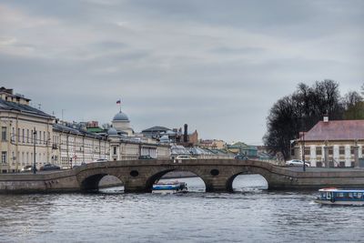 Bridge over river in city against cloudy sky