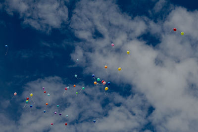 Low angle view of helium balloons flying in cloudy sky